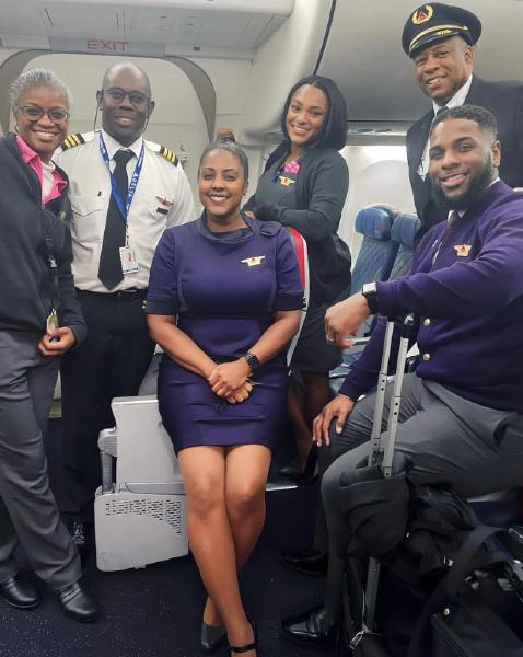 A picture of six Black people in Delta Airlines uniforms, a mix of crew and pilots, posing for a picture inside an airplane.