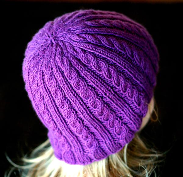 A very purple kit hat with ribs and braids, extending beyond the ears, shaped somewhat like a thimble, worn by a person facing away, with long straight hair emerging below the hat.