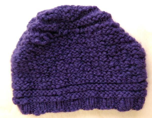 A dark blue hat knit in garter stitch, lying flat against a white backgrond.