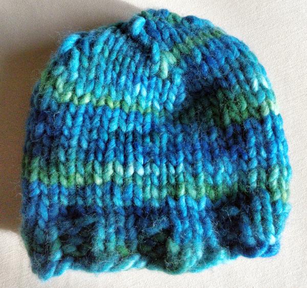 A knit hat, either very small or of very bulky yarn, with multiple shades of blue and green circling through.