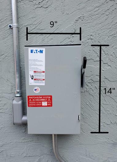 A gray metal box attached to a gray stucco wall.  Black dimension bars drawn on the picture show it is 9 inches wide and 14 inches high.  A metal conduit emerges from the bottom left corner of the box and extends up beyond the top of the picture.  Another metal conduit emerges from the bottom center and extends downward.